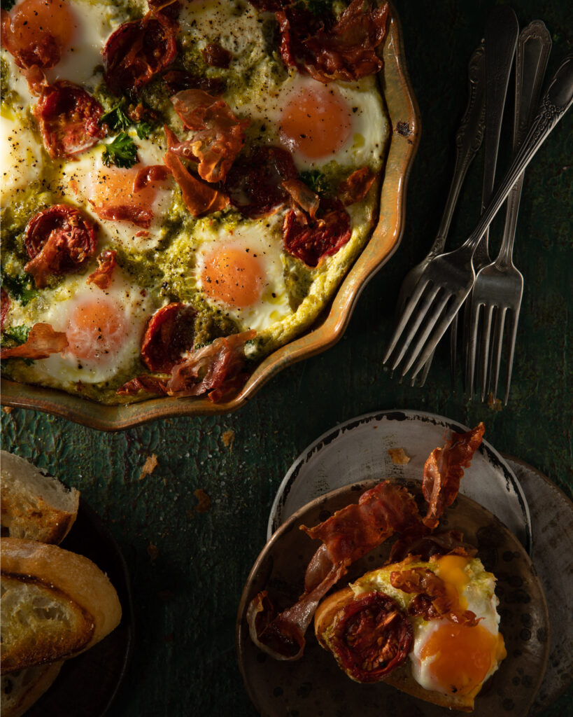 An easy breakfast bake made with eggs, presented in a pie dish in the upper left corner, with a piece on a plate, and forks to the right of the pie dish.