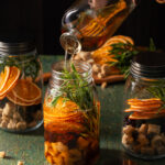 A mason jar filled with whiskey, oranges, sprigs of spices, and much more.