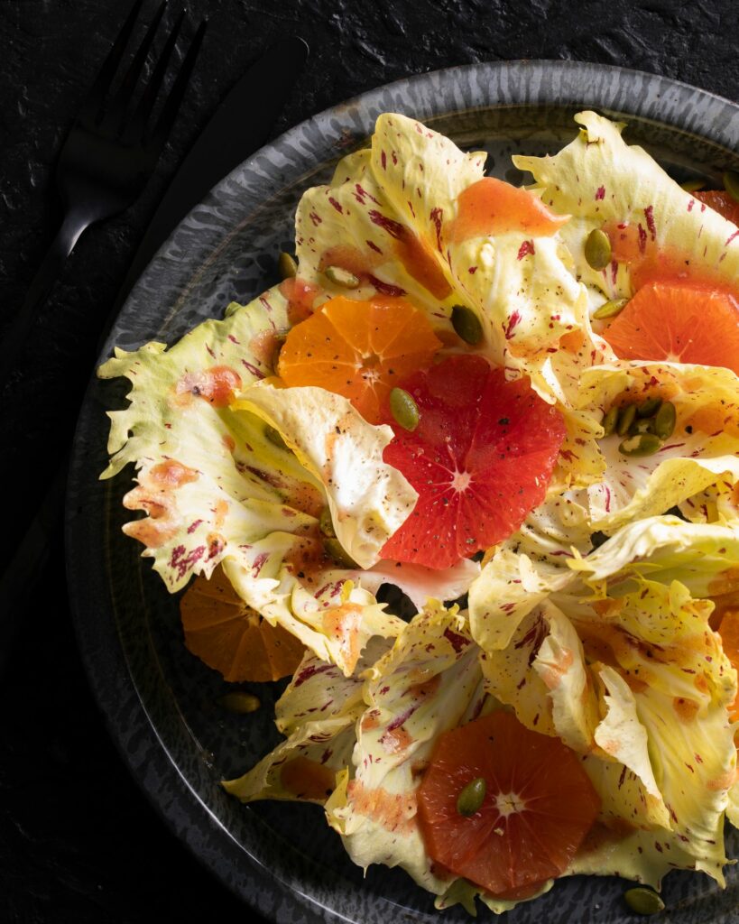 A close up picture of bitter green leaves littered with sliced fruit in the bitter greens salad.