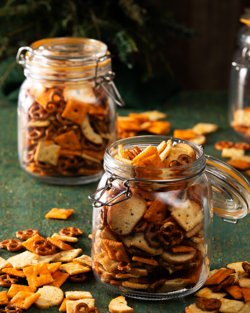 Two big mason jars filled with a salty snacks mix like chips, pretzels, and more.