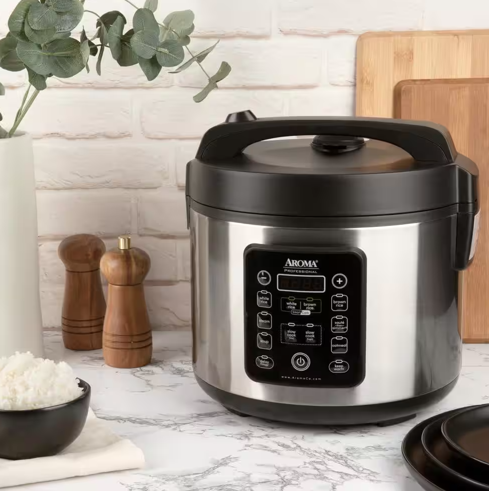 A silver and black digital rice cooker sits on a marble counter next to cutting boards, salt and pepper shakers, and a bowl of rice.