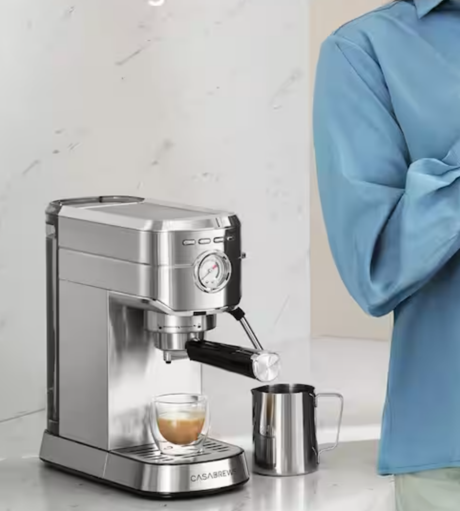 A silver espresso machine with a shot of espresso underneath and a milk carrier beside it.