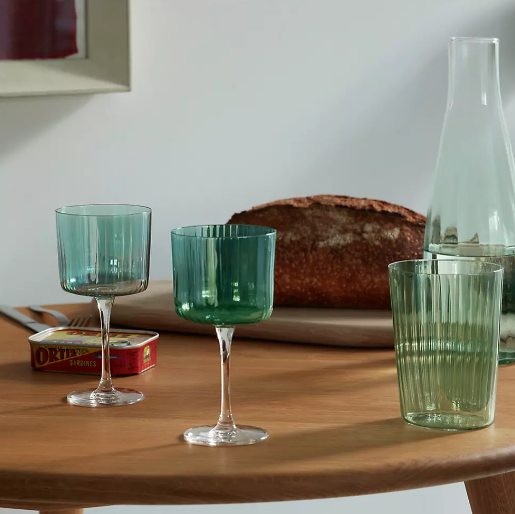 A set of green opaque wine glasses perfect for a home bar sit on a brown dining table.