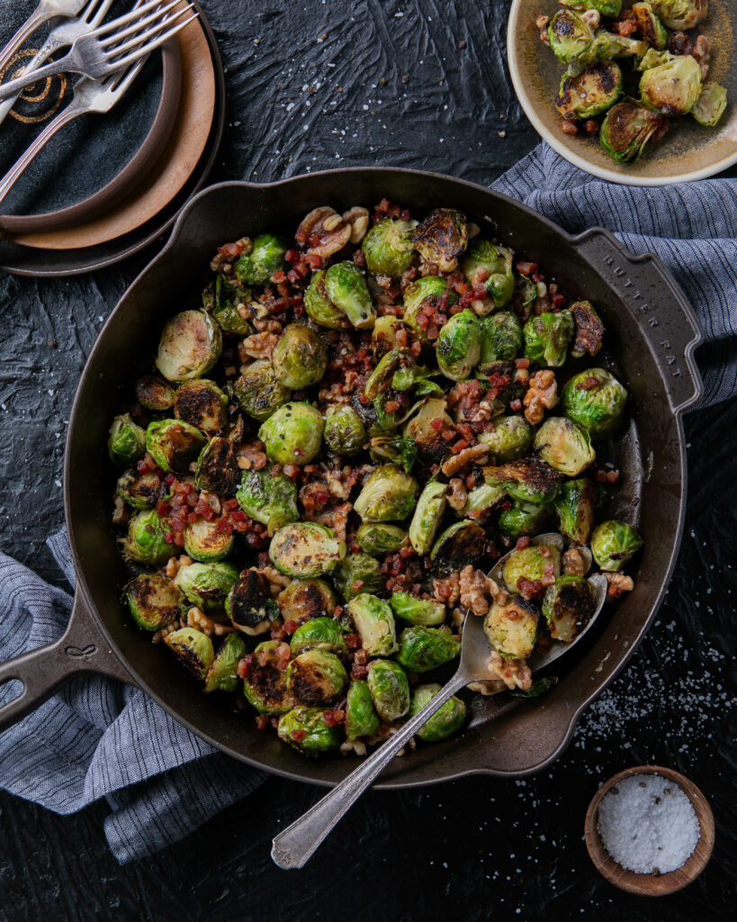 Seared brussels sprouts in a cast iron pan with walnuts and pancetta.