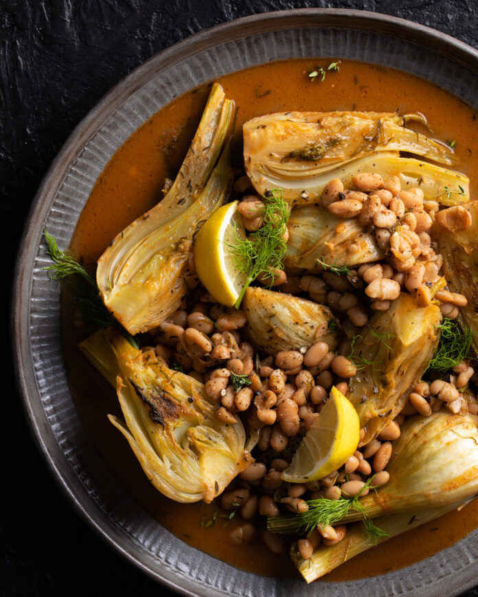 A round gray dish with braised fennel and white beans sitting in a broth.