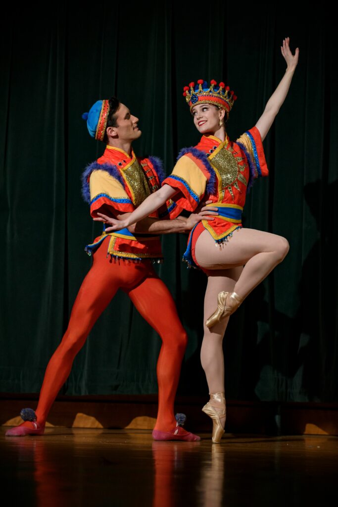 Two dancers dressed in colorful red, yellow, and blue outfits striking a pose on stage.