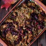 A stuffing dish filled with cranberries and celery surrounded by leaves and green apples.