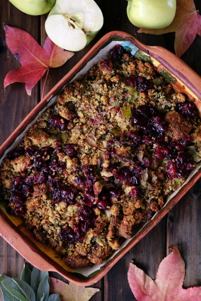 A stuffing dish filled with cranberries and celery surrounded by leaves and green apples.