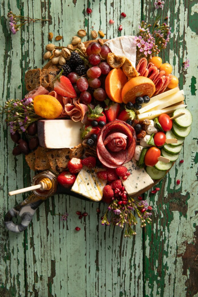 A Pittsburgh party tray sits on a green table filled with fresh vegetables, fruits, meals, and cheeses formed in a circle.