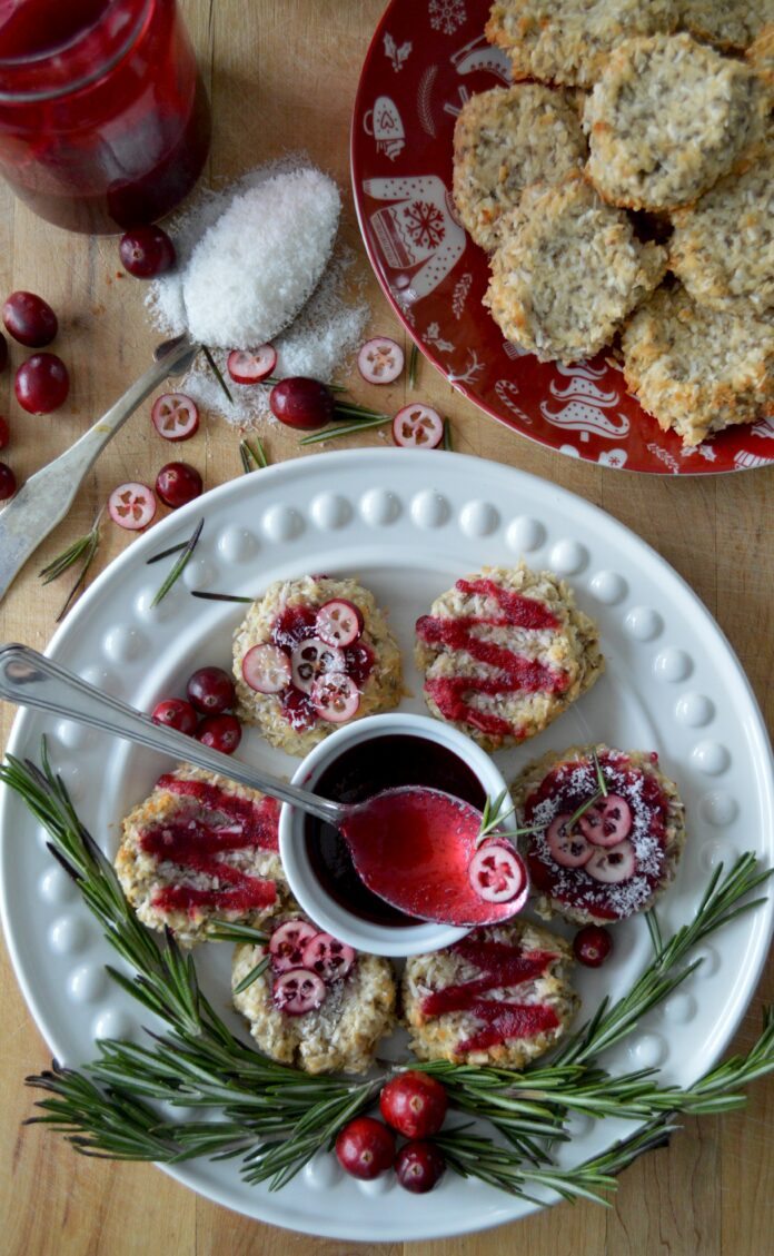 An aerial view of a six cookies drizzled with a red glaze and covered with cranberries.