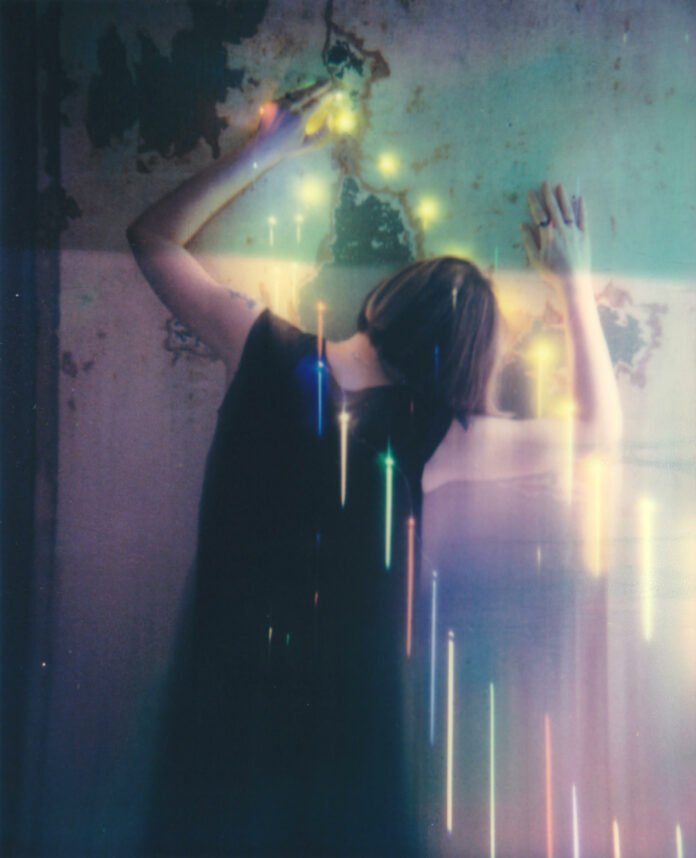 the back of a woman's body, her hands against a wall, with lights and colors streaming down the frame