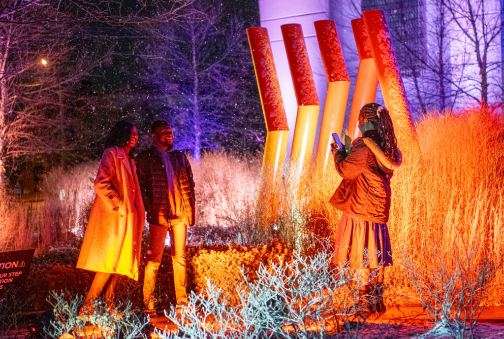 Two parents get a photo taken by their daughter in front of orange lights outside.