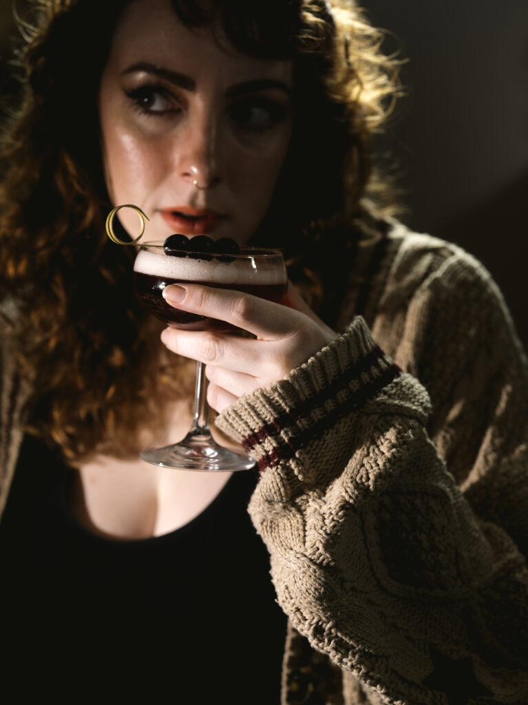 A woman sips a cocktail with a topping of black orbs.