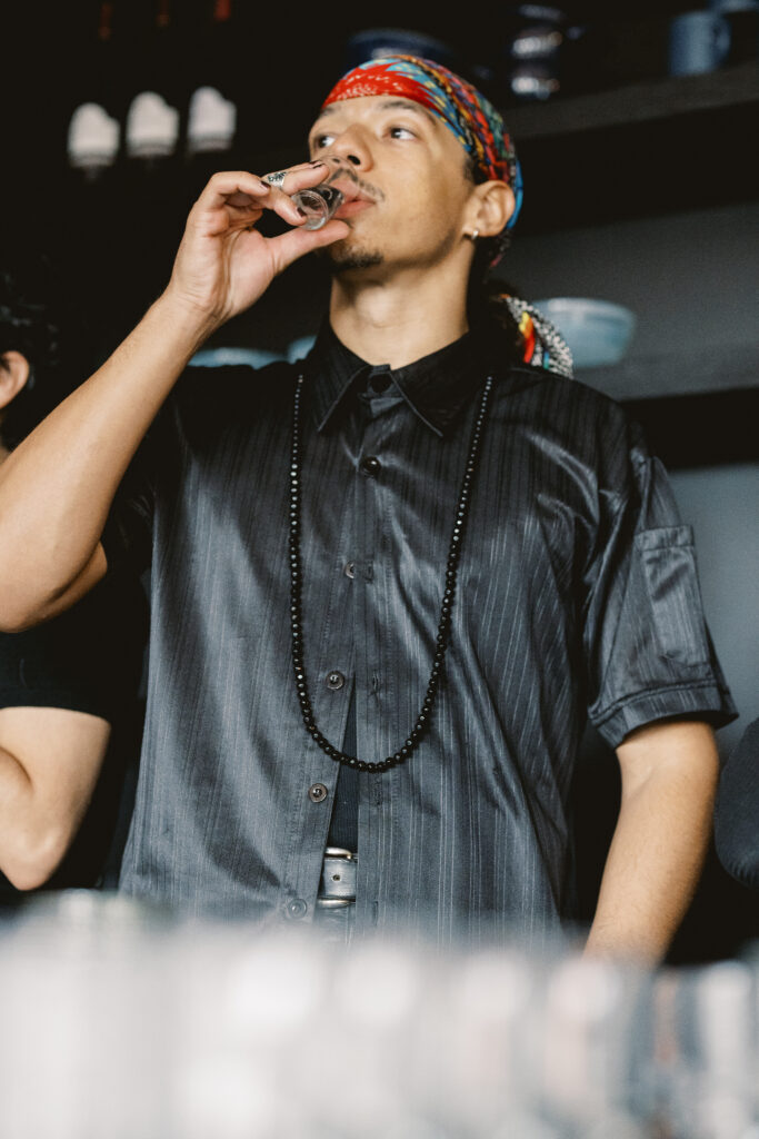 A man in a black shirt and colorful bandana taste tests a liquor at a local distillery in Pittsburgh.