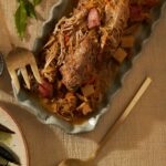 Oven braised pork in a pan mixed with sauerkraut and other components with a fork and spoon nearby.