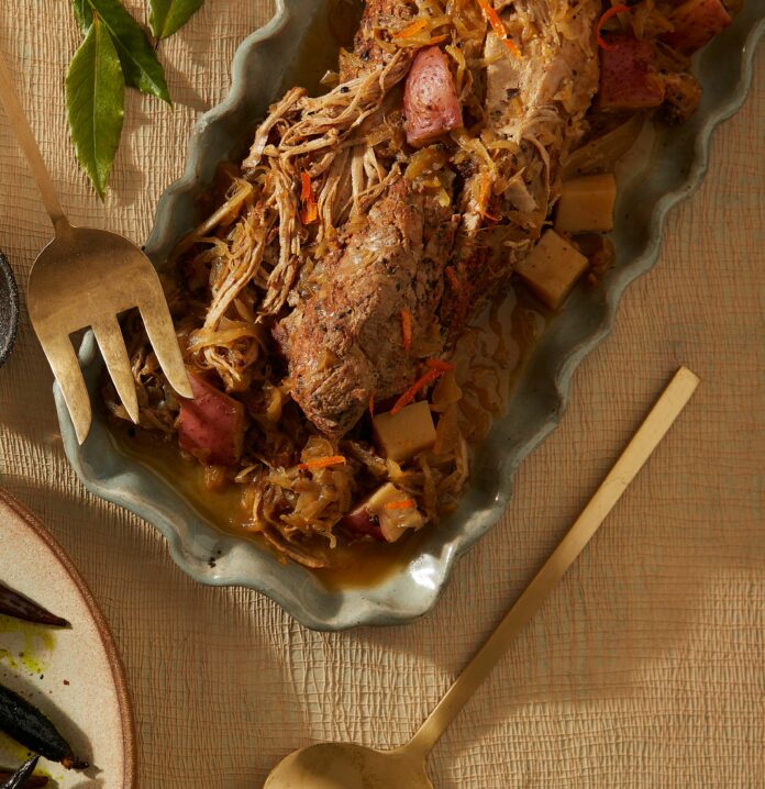 Oven braised pork in a pan mixed with sauerkraut and other components with a fork and spoon nearby.