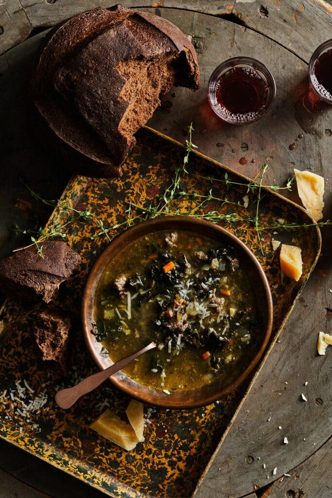 A brown table with a tray on top featuring a brown dish of Italian Lentil Soup with bread and spices spread around the outside of the bowl.