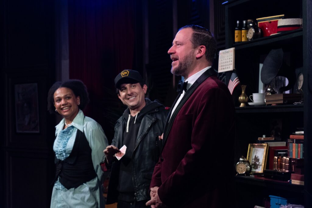 Three people stand at the front of a comedy stage with smiles on their faces, looking at one another in Pittsburgh.