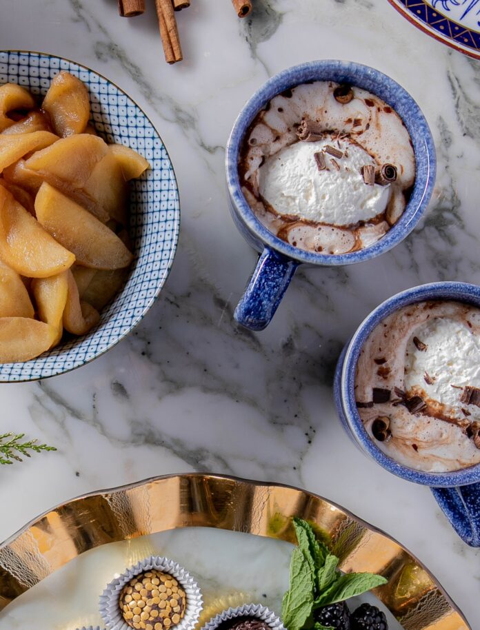 Two mugs filled with fresh orange-spices horchata with plates of food nearby.