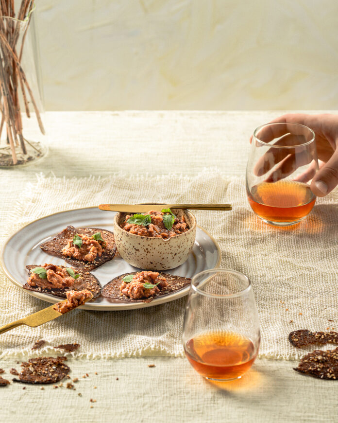 A dish of rye crisps topped with tomato ragout and wine glasses surrounding the dish.