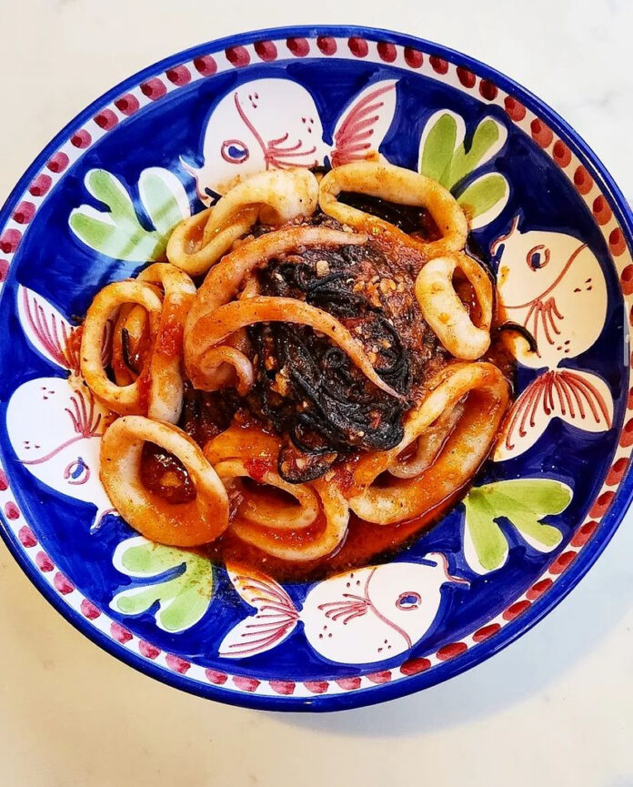 Seven Fishes A dish. of octopus and pasta prepared on a blue plate with floral designs on it.