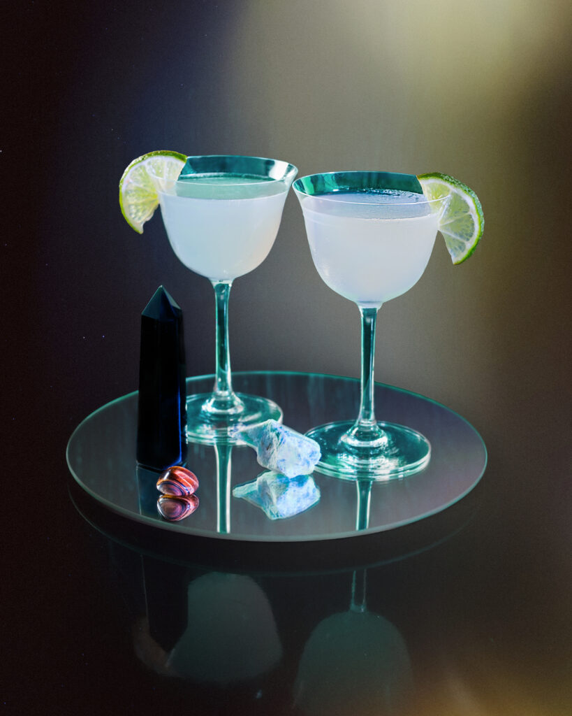 A cocktail for gemini that's two glasses filled with an iridescent liquid and topped with a lime.