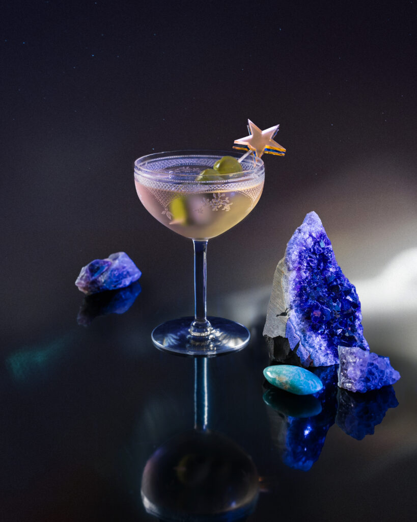 A gin Martini cocktail for Virgo on a tabletop with a star topper in the glass and purple amethyst on the table.