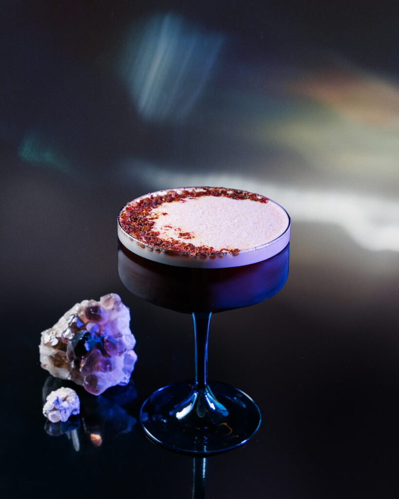 A espresso martini cocktail for Sagittarius sits in a glass, topped with espresso powder with a crystal gem to the left.