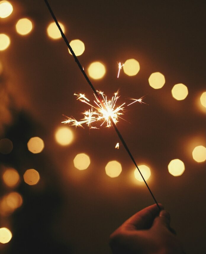 Your New Year's Resolution Horoscope for 2025 A person holds a New Years sparkler in front of strings of yellow lights.