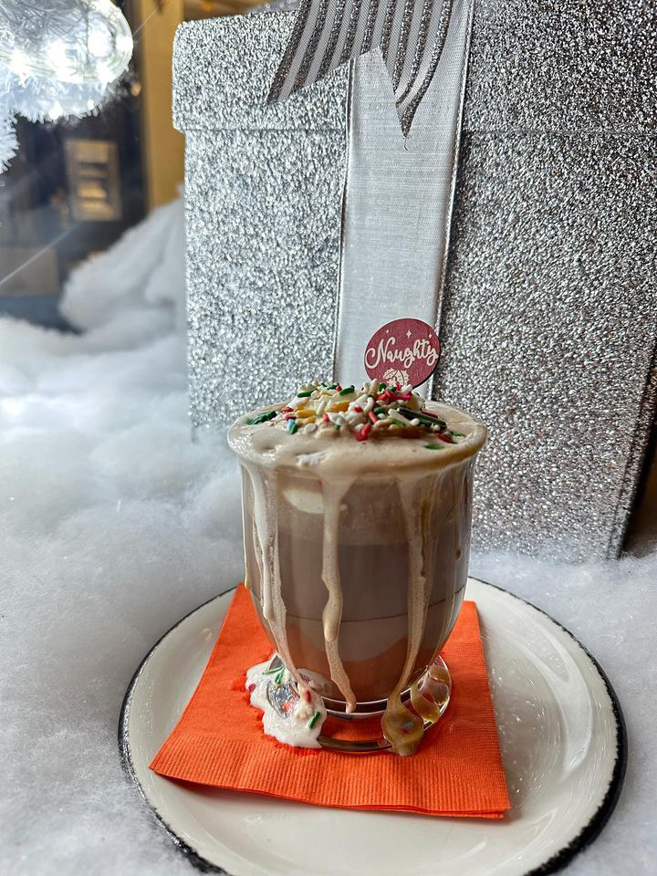 A glass of alcoholic hot chocolate overfilling in front of a white present and fluffy cloud snow in Ritual House in Pittsburgh.