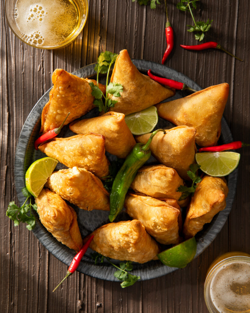 a blue plate filled with turkey samosas from kilimanjaro flavour. limes and peppers are also placed throughout the plate.