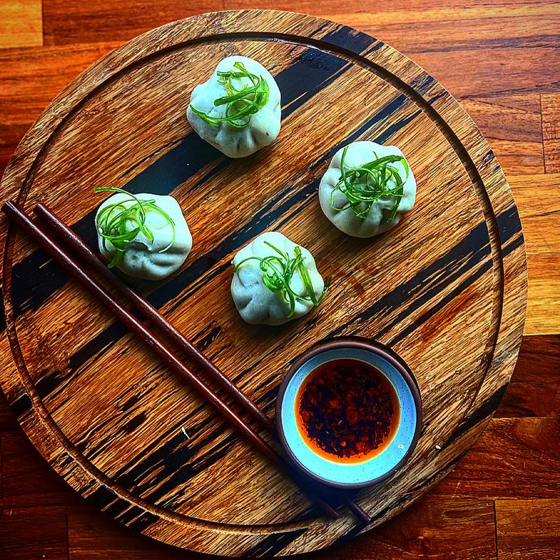 Four stuffed bao buns from EYV in pittsburgh sit on a wooden tray next to chopsticks and a container of sauce.