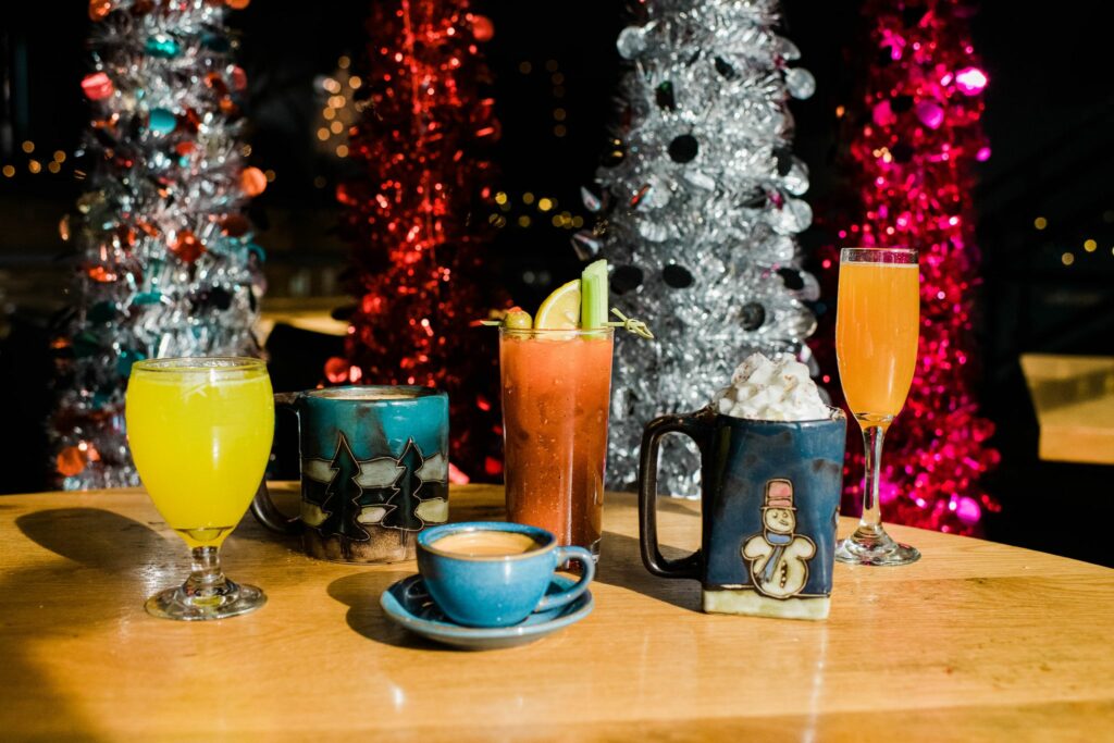An array of colorful winter themed drinks from Square Cafe restaurant in Pittsburgh sit on a wooden table in front of red and silver christmas trees.