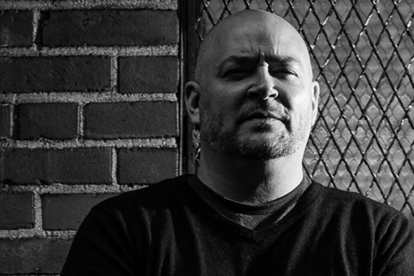 David Throckmorton stands in front of a fence and brick wall pictured in black and white.