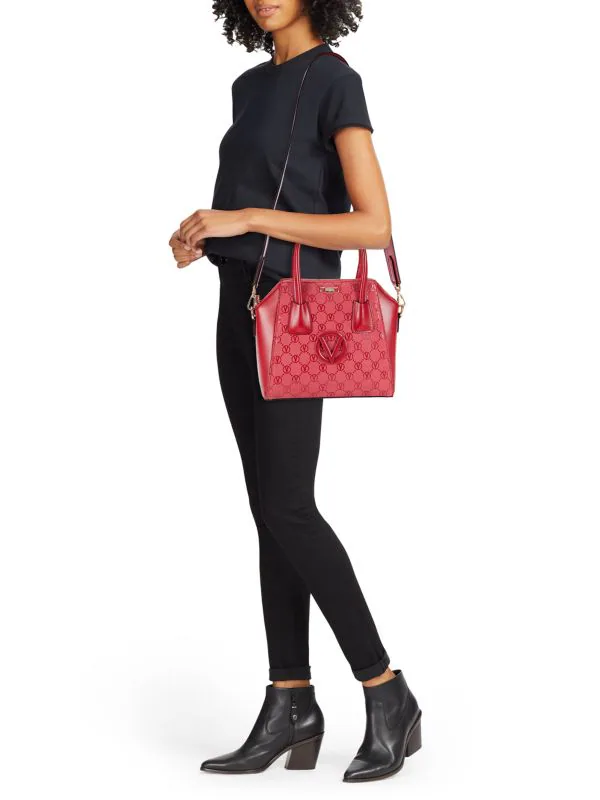 A woman in all black carries a bright red Mario Valentino shoulder bag with a V monogram on the front.