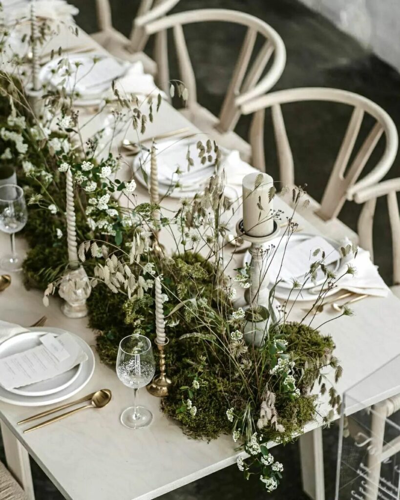 A white table setting with plenty of wildflower accessories, candles, and plate settings. White chairs also surround the table.