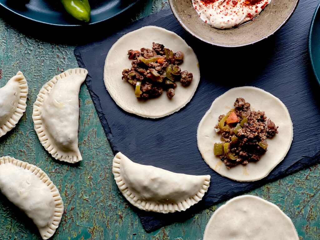 Small Circles of raw dough with meat and veggie filling, and half moon shaped hand pies that are also uncooked.