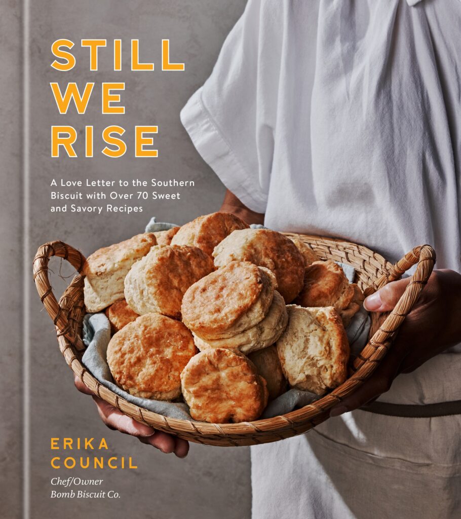 A cookbook cover for Still We Rise pictures a person in white clothing holding a basket of fresh baked biscuits.