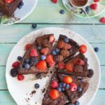 An overhead photo of a chocolate cut cut into wedges with berries, on a blue wooden surface.