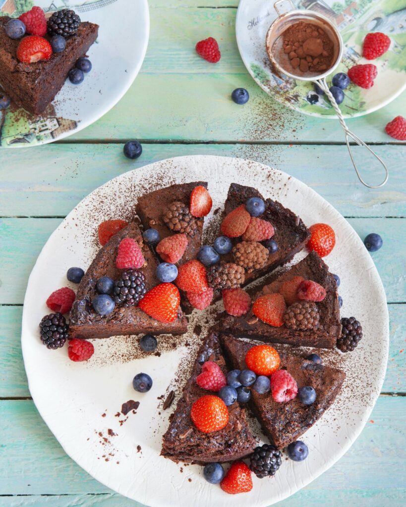 An overhead photo of a chocolate cut cut into wedges with berries, on a blue wooden surface.