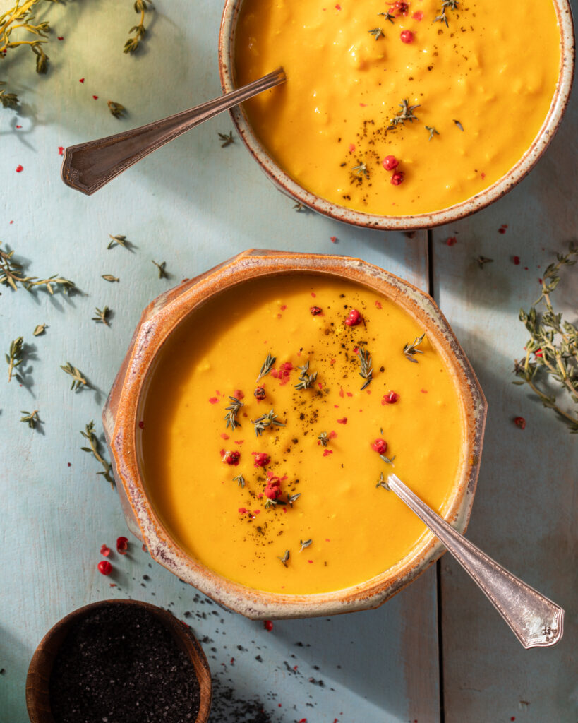 Two soup bowls filled with orange butternut squash soup topped with shredded leaf garnishes and a spoon.