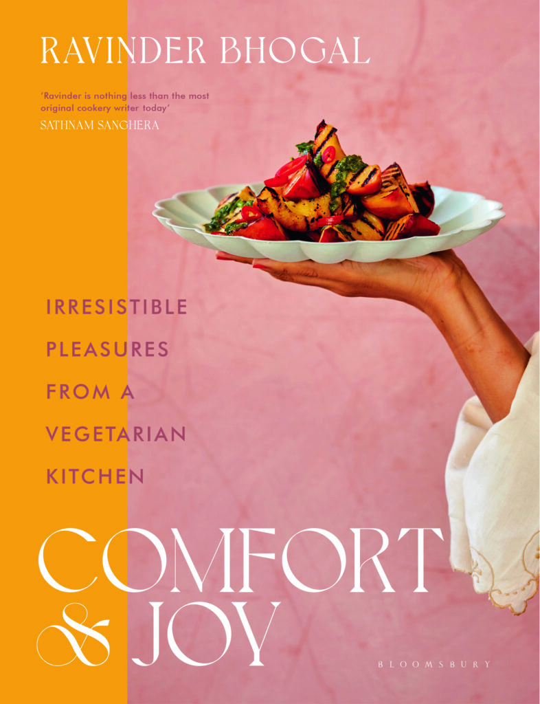 A woman holds a fancy white plate of vegetables against a pink and orange background for the best 2023 cookbook, Comfort and Joy.