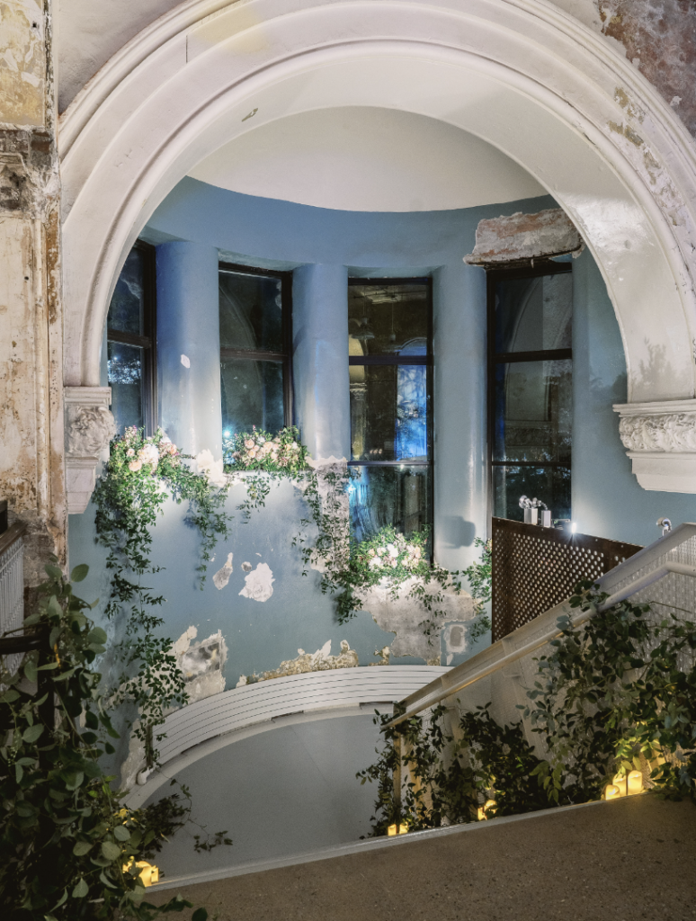 An open stair space with a huge white arching ceiling is decorated in various vines and other greenery.