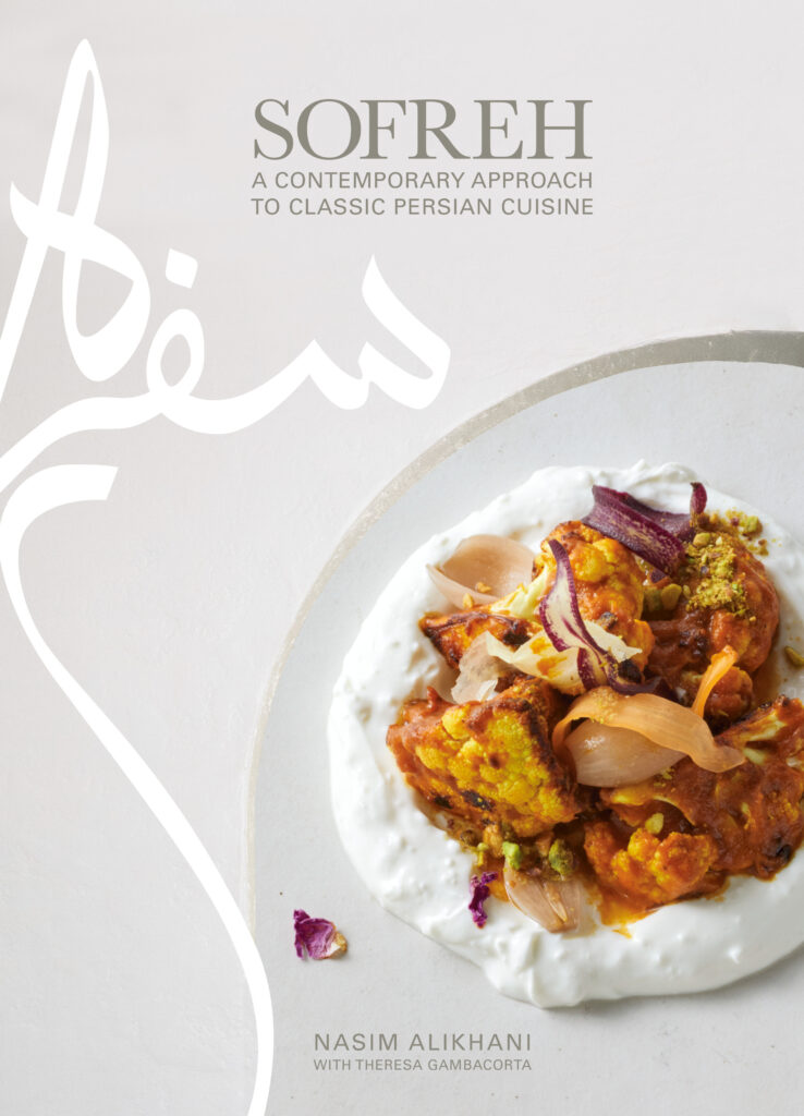A white cover of a 2023 cookbook displays a white plate with various proteins and vegetables on top. The name "Sofreh" is painted across the top left corner.