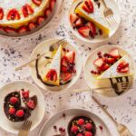 An overhead photo of a Lemon Saffron Tort in the upper left corner, three cream colored plates with slices of the tort with berries, and chocolate tarts at the bottom of the photo.
