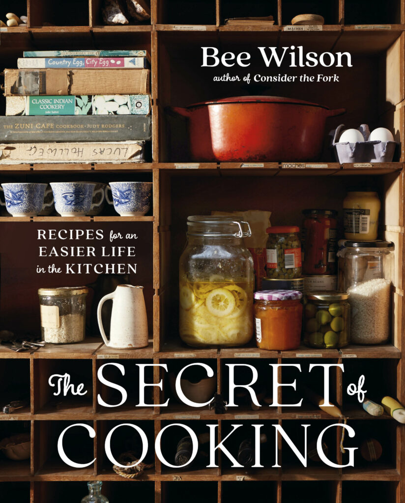 A cookbook cover displays shelves filled with kitchen materials like jars of ingredients.