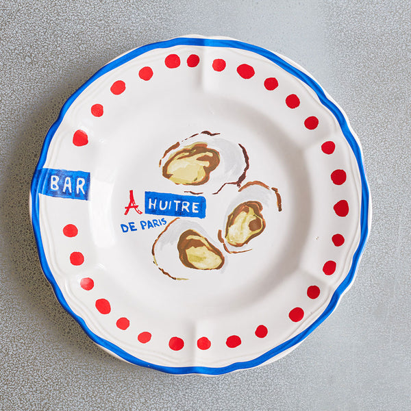 A white plate with red dots around the outside, blue paint around the brim, and French designs in the center.