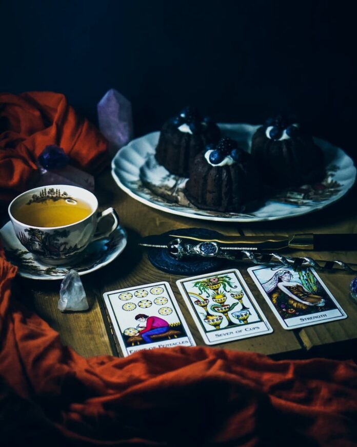 Chocolate cake served in a plate alongside tarot cards and a cup of tea