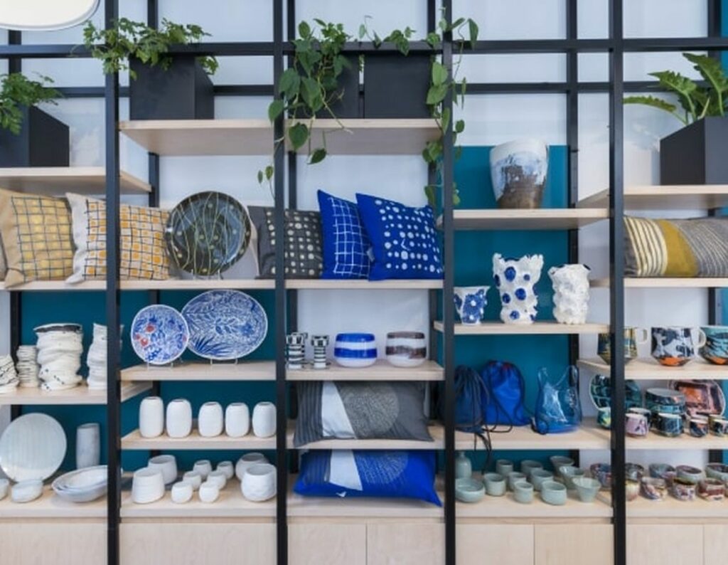 A display of shelves filled with blue and white items for the kitchen like plates and vases and for the living room like pillows all at Empreintes