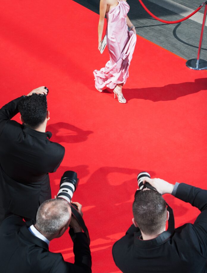A women in a pink dress on the red carpet being photographed by the paparazzi.